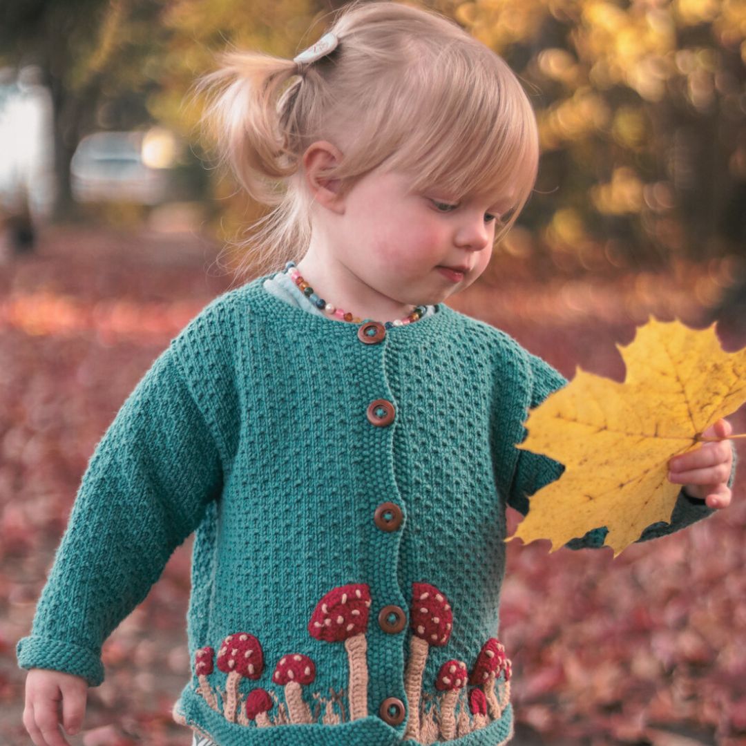 Hand knitted gender-neutral children's cardigan with mushroom motifs.
