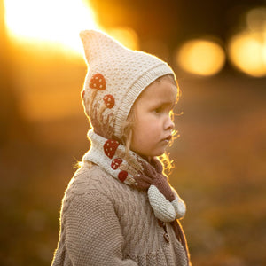 Toddler wearing hand-knit mushroom neck scarf in creamy light green cotton bamboo, artisan-made kids mushroom accessories.