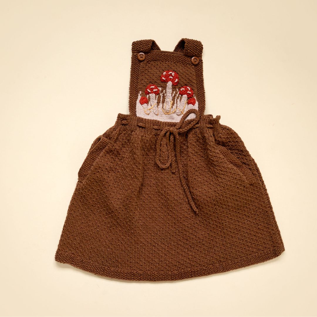 Flat lay of hand-knit mushroom pinafore in chocolate brown cotton bamboo, artisan-made baby girl mushroom outfit by JuneBee Baby.