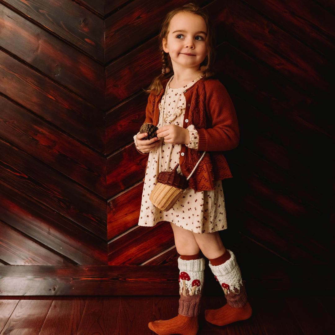 Child wearing hand-knit mushroom leg warmers in creamy light green cotton bamboo, artisan-made slow fashion knitwear.