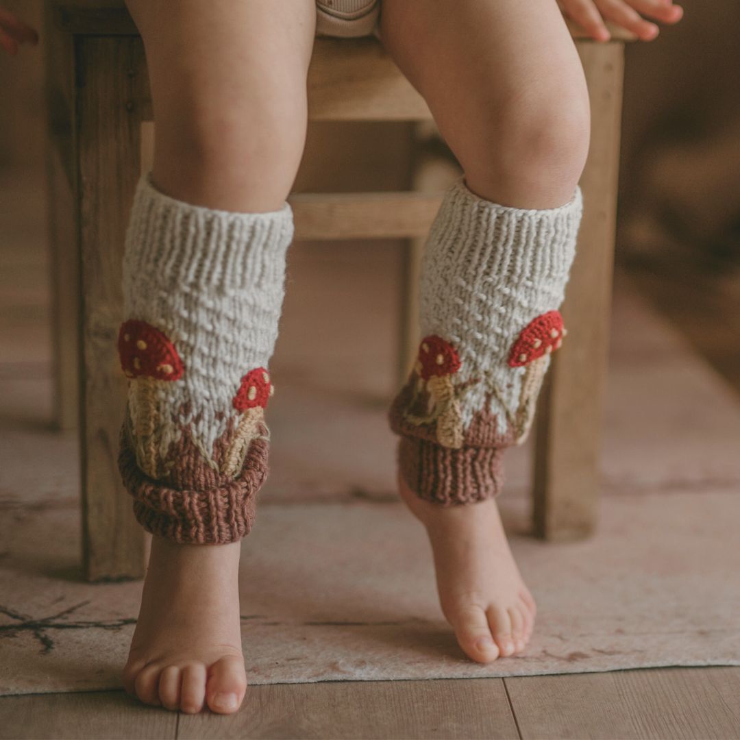 Toddler wearing unisex hand-knit mushroom leg warmers in creamy green cotton bamboo, mushroom baby stuff for kids by JuneBee Baby.
