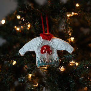 Hand-knit mushroom sweater ornament in creamy light green cotton hanging on a Christmas tree, artisan-made mushroom Christmas ornament by JuneBee Baby.