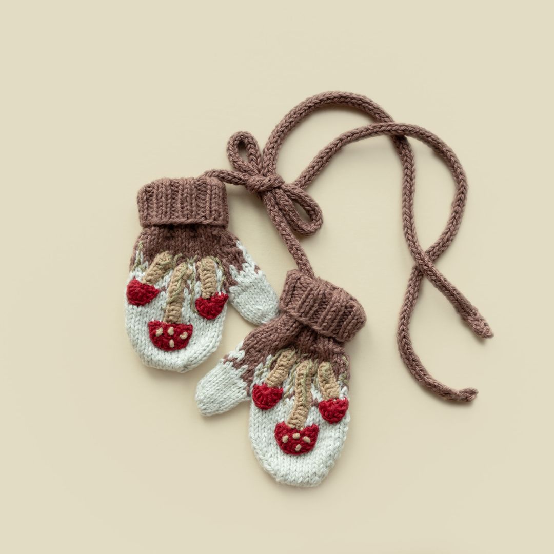 Flat lay of hand-knit mushroom mittens in creamy light green cotton bamboo, artisan-made kids mushroom accessories.