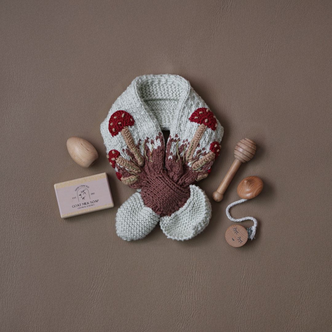 Close-up flat lay of hand-knit mushroom neck scarf in cotton bamboo showing whimsical mushroom motif detail.