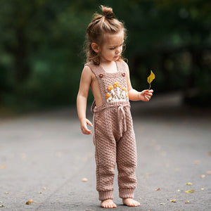 Toddler wearing hand-knit mushroom romper in blush brown cotton bamboo with adjustable criss-cross straps.
