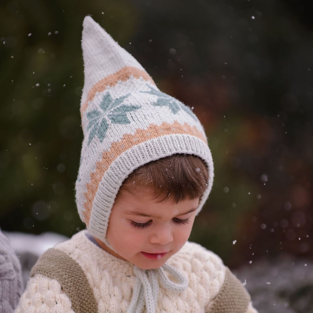 Boy wearing unisex Nordic pixie hat in creamy green hand-knit cotton bamboo with snowflake motif.